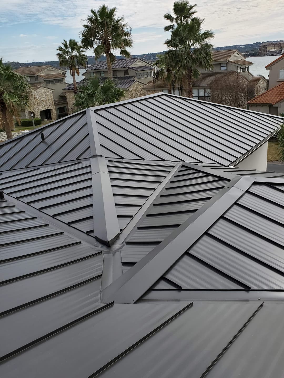 Metal roofing on modern homes with palm trees and a lake in the background.