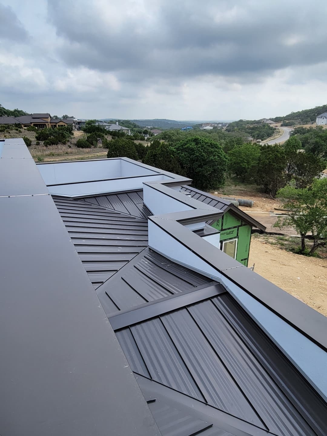 Metal roofing installation on a modern home with a view of the landscape and cloudy sky.