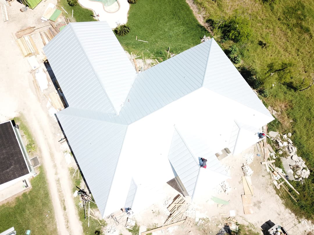 Aerial view of a house with a new metal roof under construction surrounded by greenery.