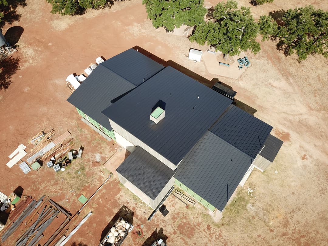 Aerial view of a large building with a metal roof, surrounded by construction materials.