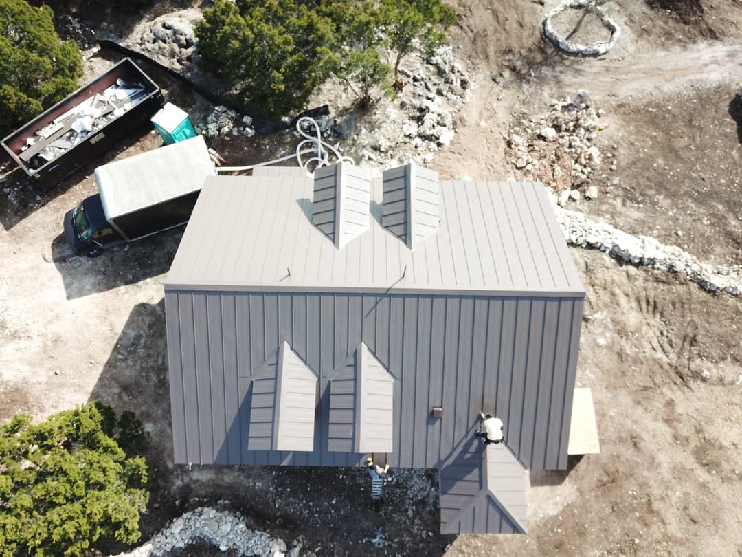 Aerial view of a modern metal roof installation on a house in a rural setting.