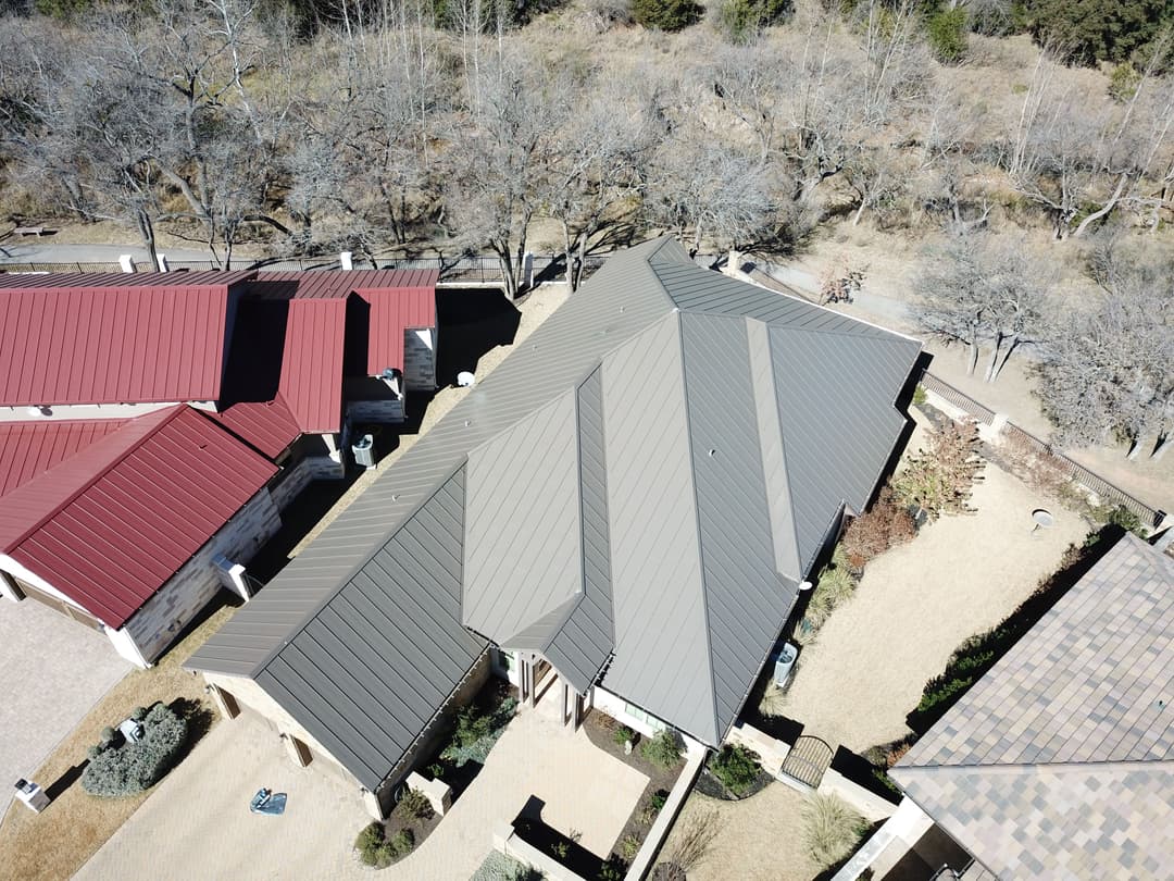 Aerial view of residential roofs with dark metal and shingle designs in a suburban area.
