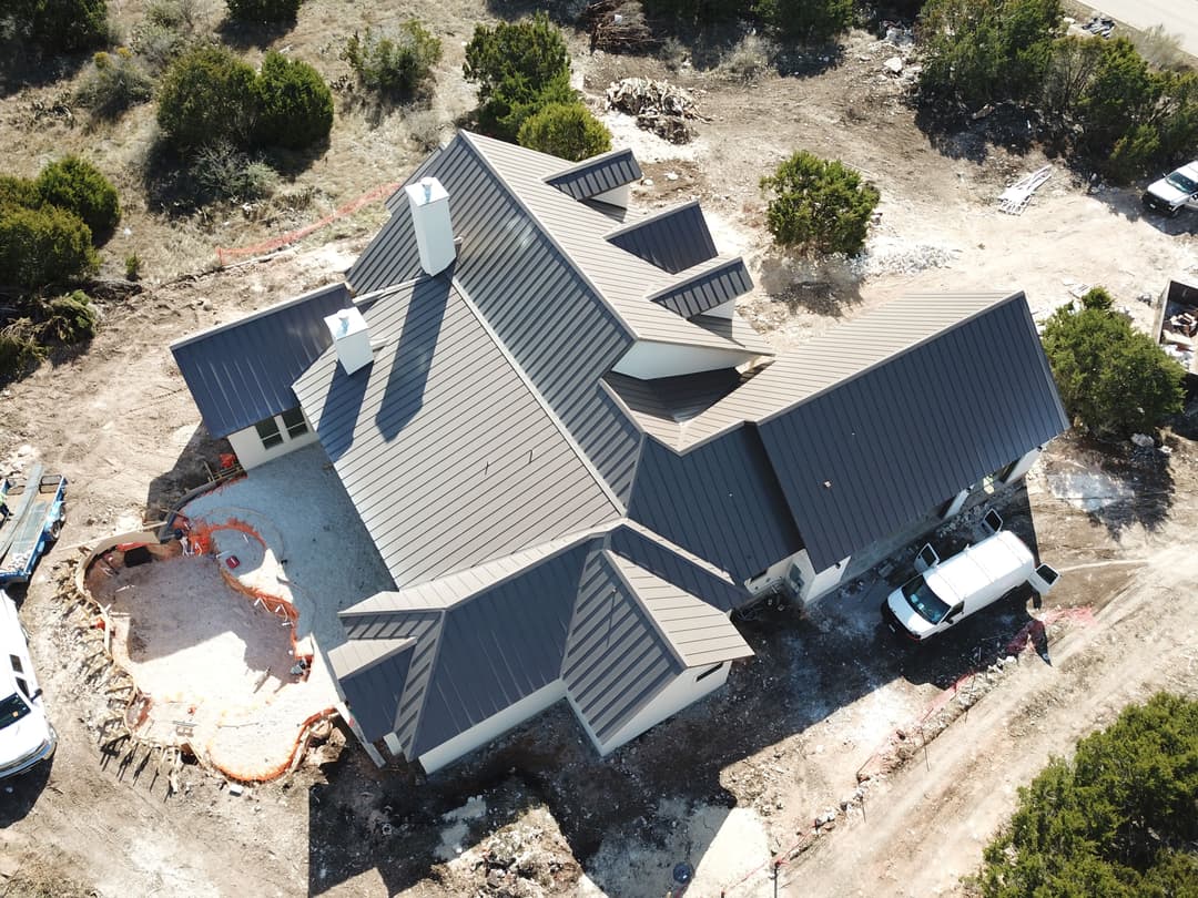 Aerial view of a modern house under construction with a metal roof in a wooded area.