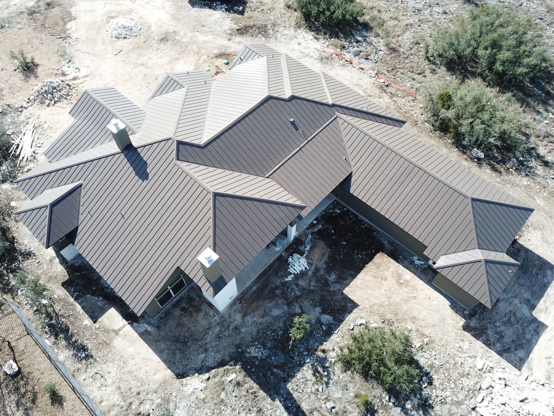 Aerial view of a modern house with a multi-pitched roof surrounded by construction site debris.