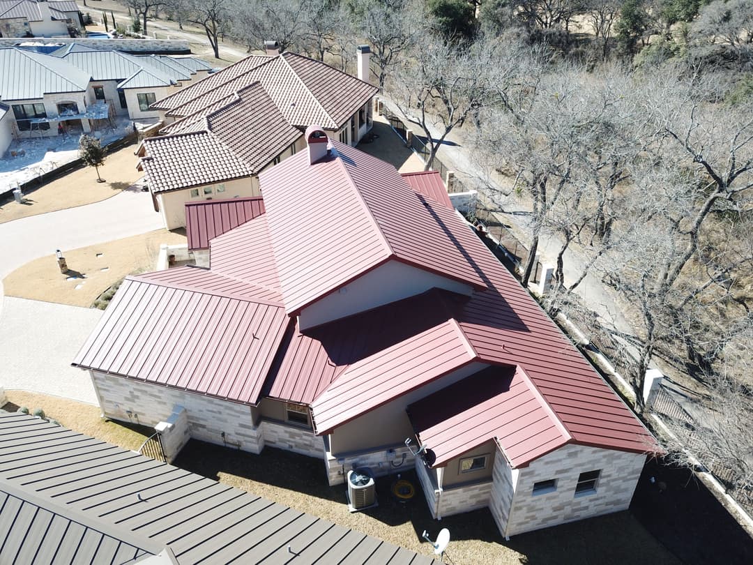 Aerial view of a modern home with a red metal roof and stone exterior in a residential area.