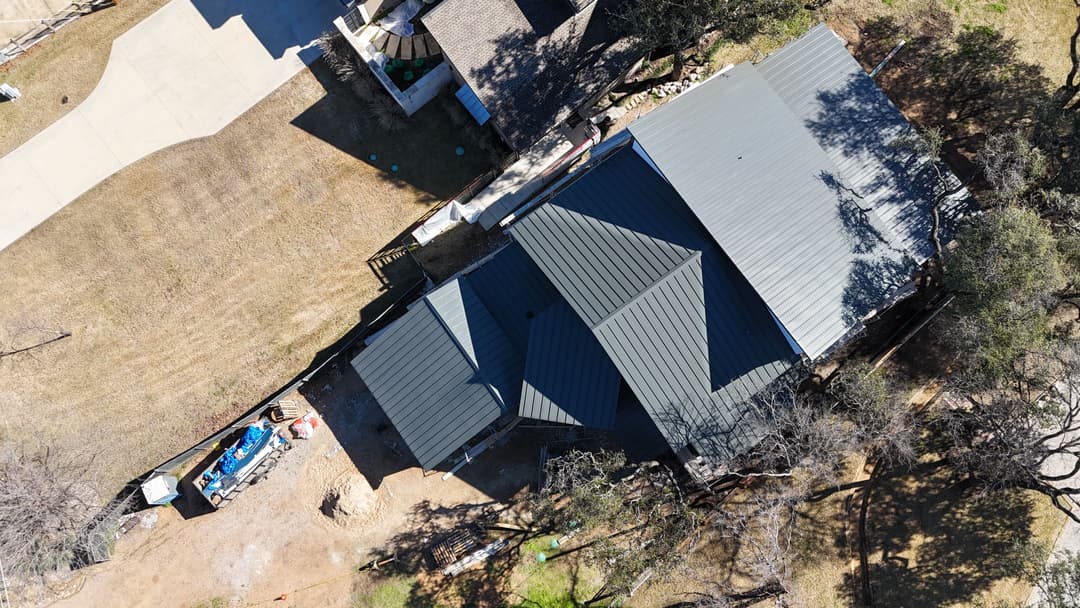 Aerial view of a green metal roof on a residential home surrounded by trees.