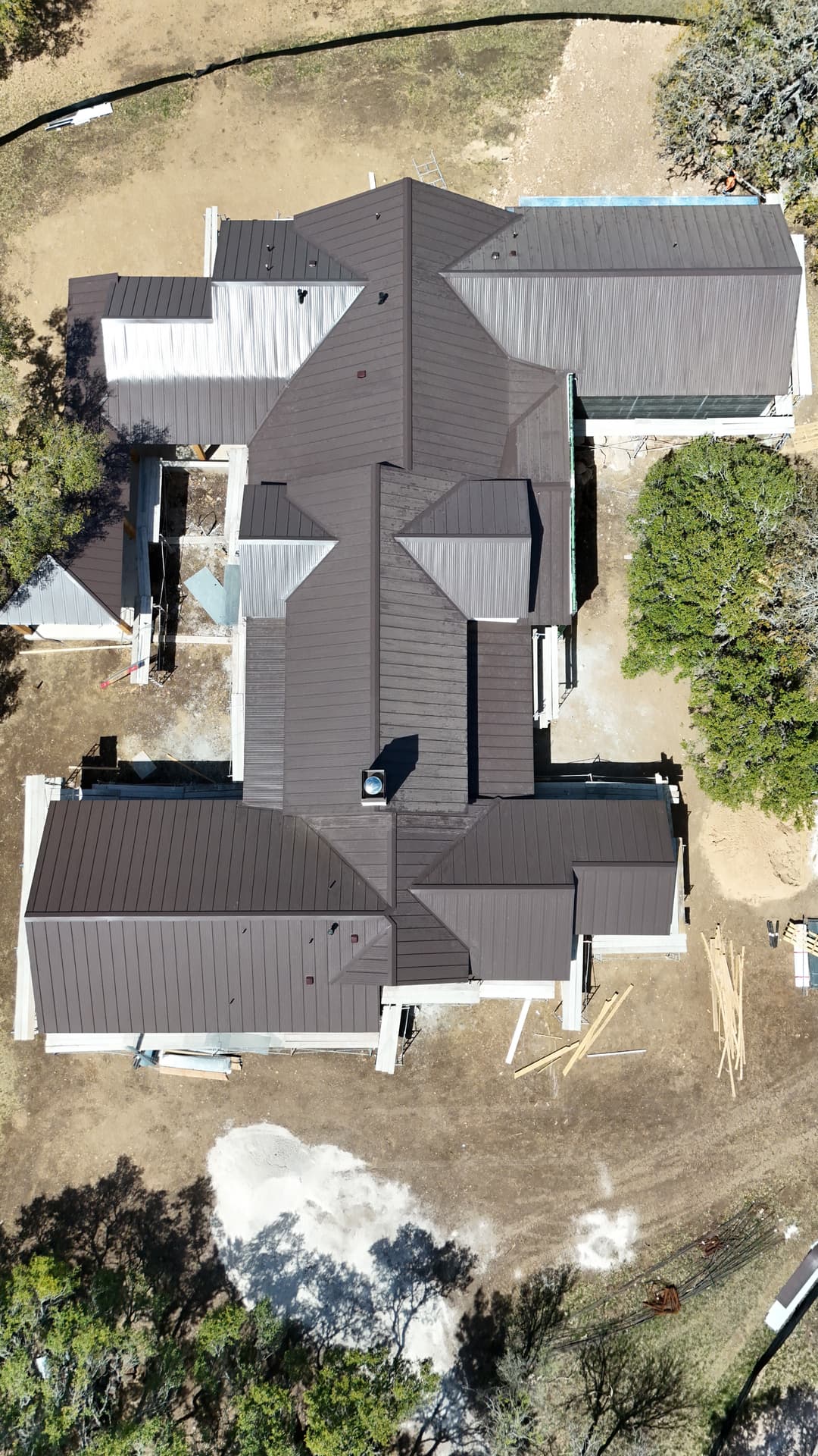 Aerial view of a large house under construction with a dark metal roof and surrounding landscape.