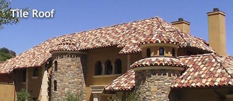 Tile roof on a stylish home featuring stone accents and a blue sky background.
