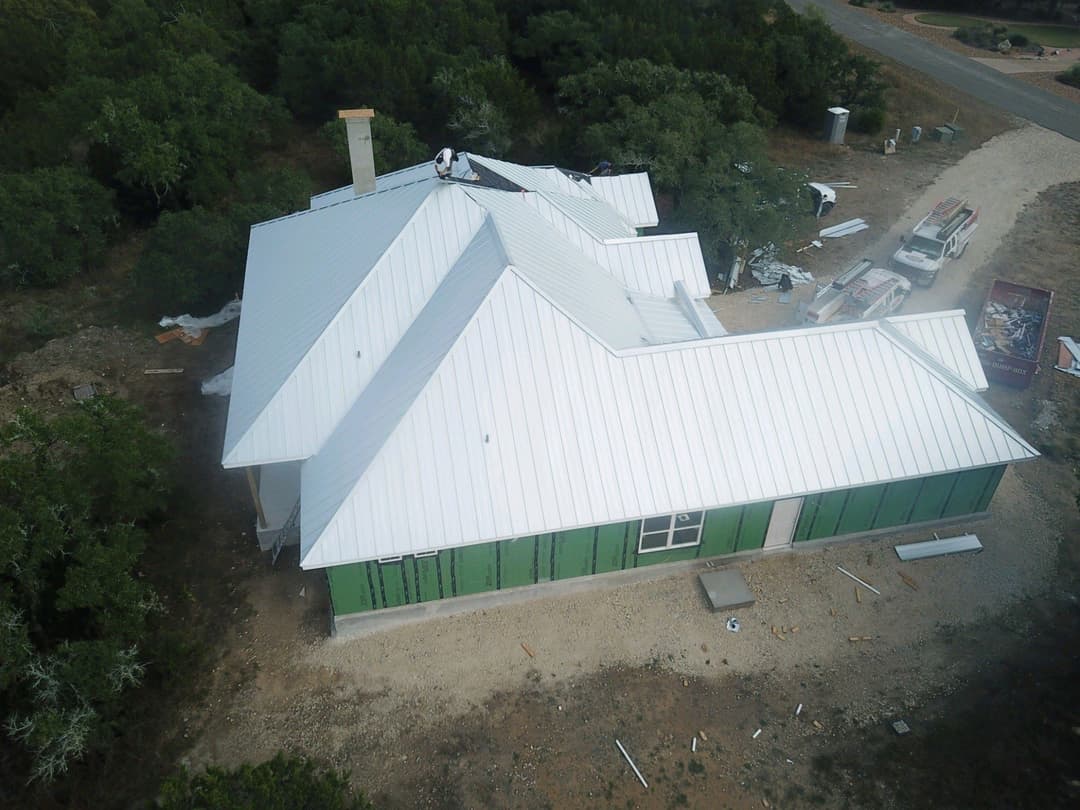 Newly constructed house with a metal roof and green siding, surrounded by trees.