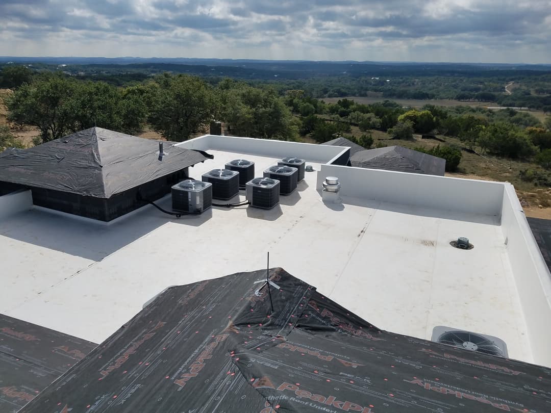 Rooftop view featuring HVAC units and a landscape of rolling hills under a cloudy sky.