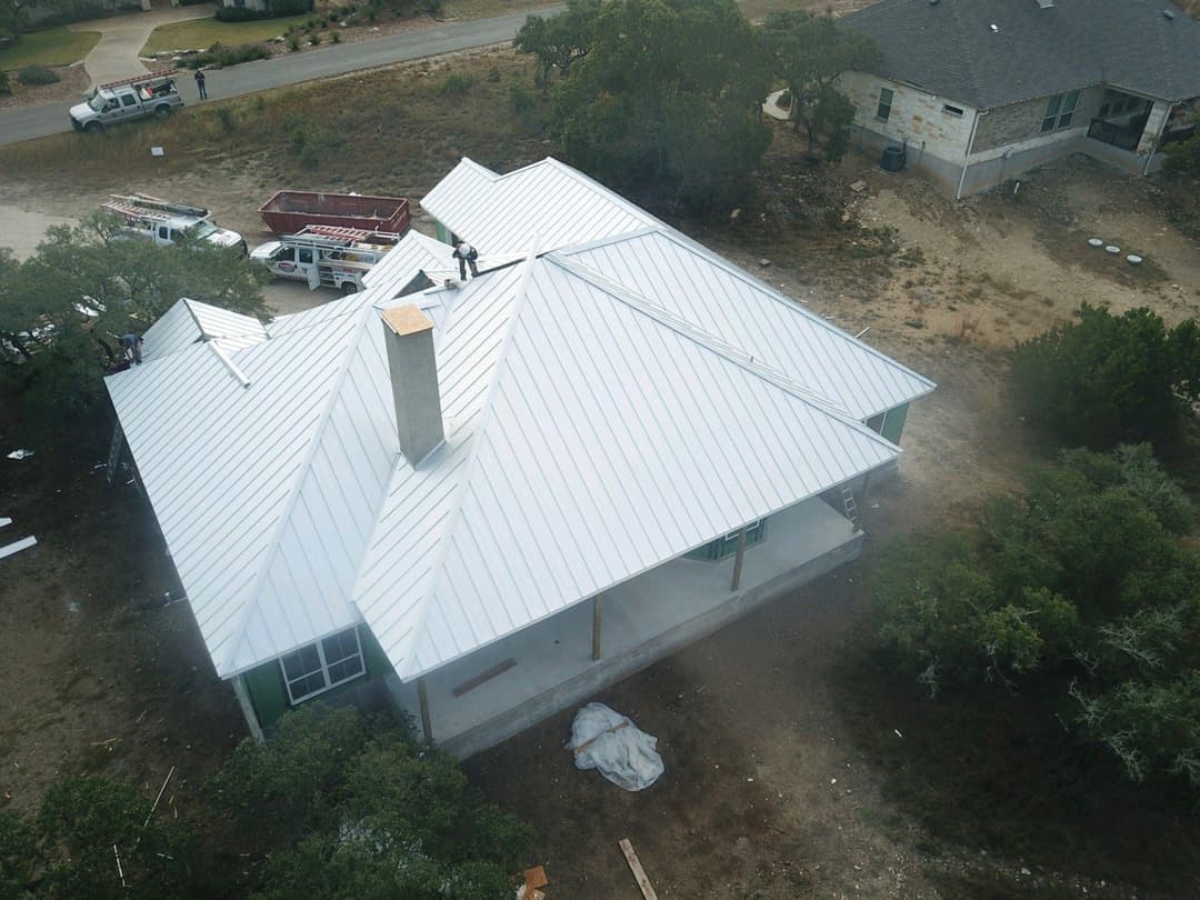 Aerial view of a newly constructed house with a metal roof and construction workers.