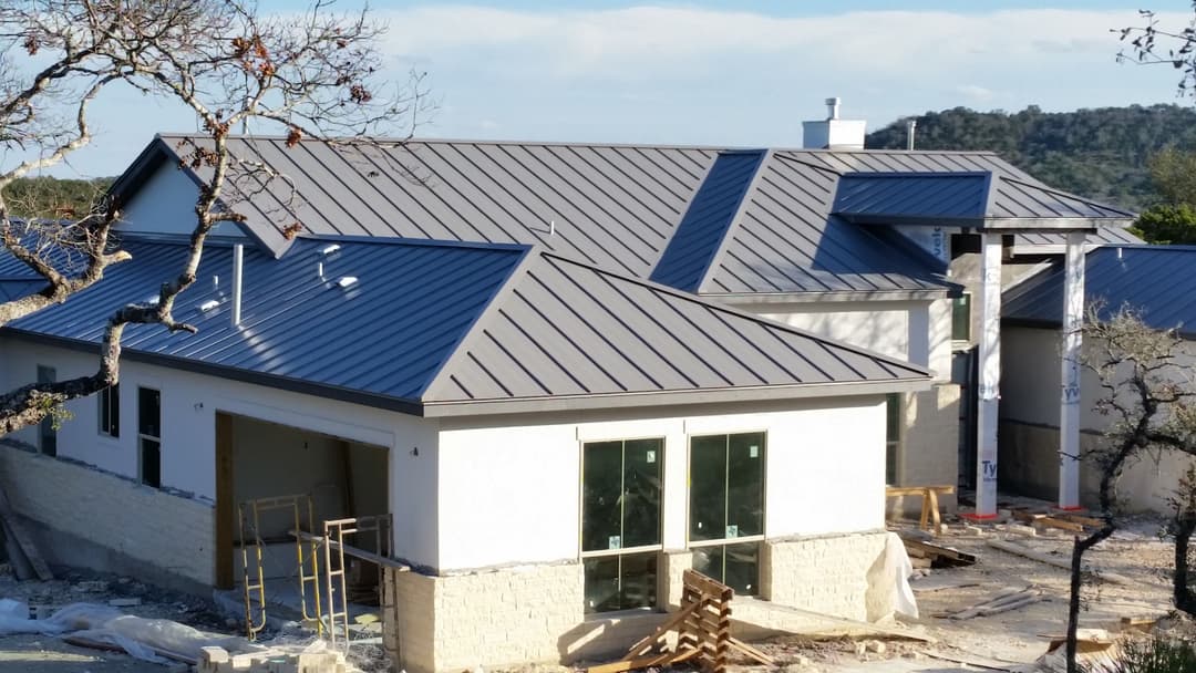 Newly constructed home with a metal roof, surrounded by construction materials and a scenic view.