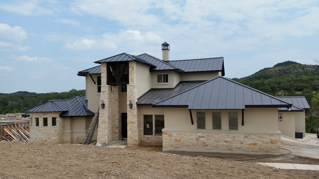 Modern two-story home with stone accents and a metal roof, set against a hilly landscape.