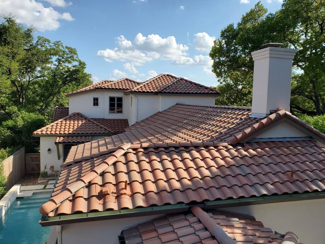View of a modern home with terracotta tile roof and swimming pool surrounded by greenery.
