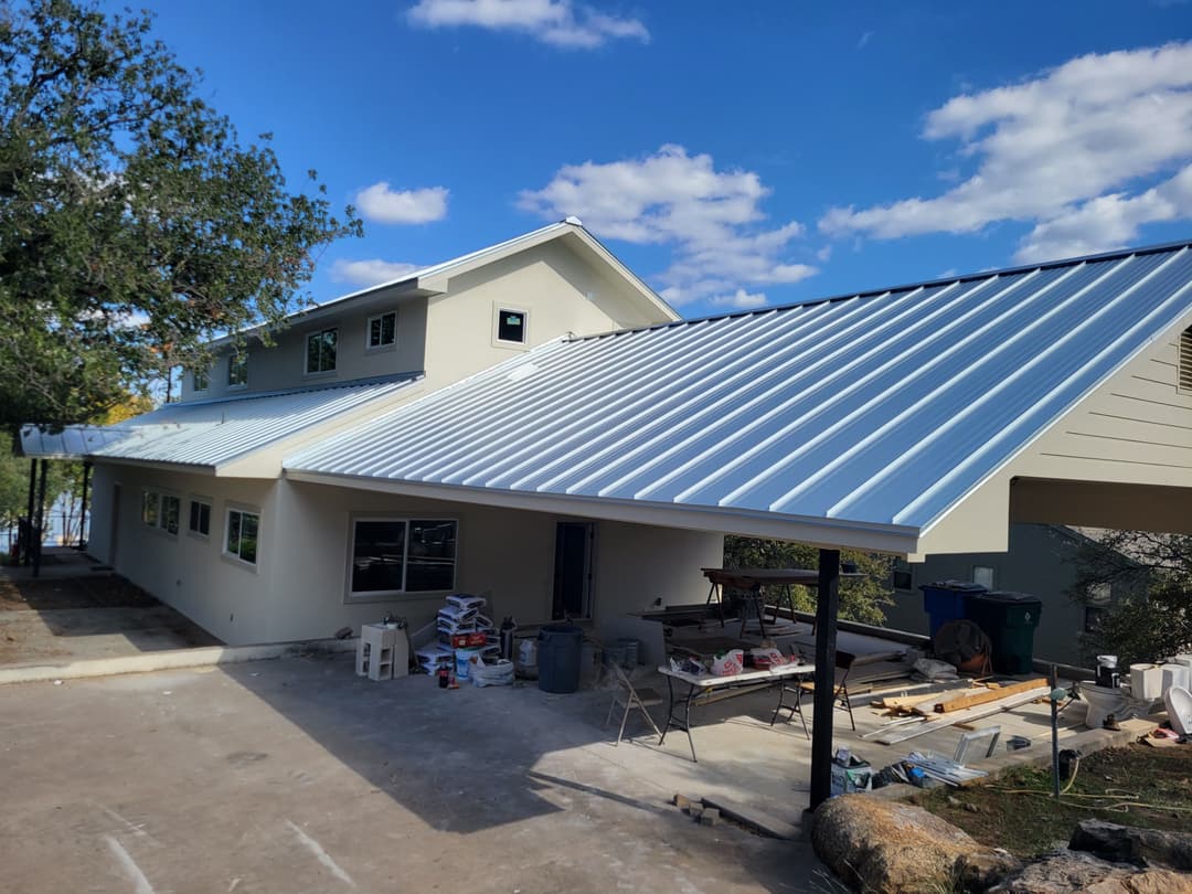 Modern home with a metal roof under blue skies, featuring construction materials nearby.