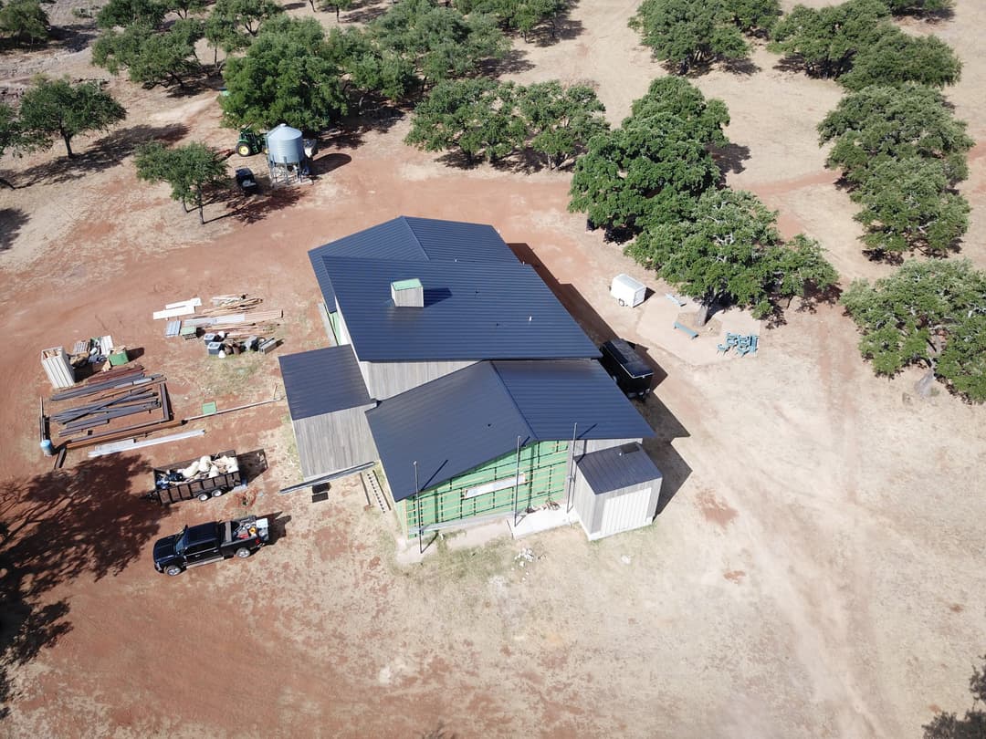 Aerial view of a modern house under construction in a rural area with surrounding trees.