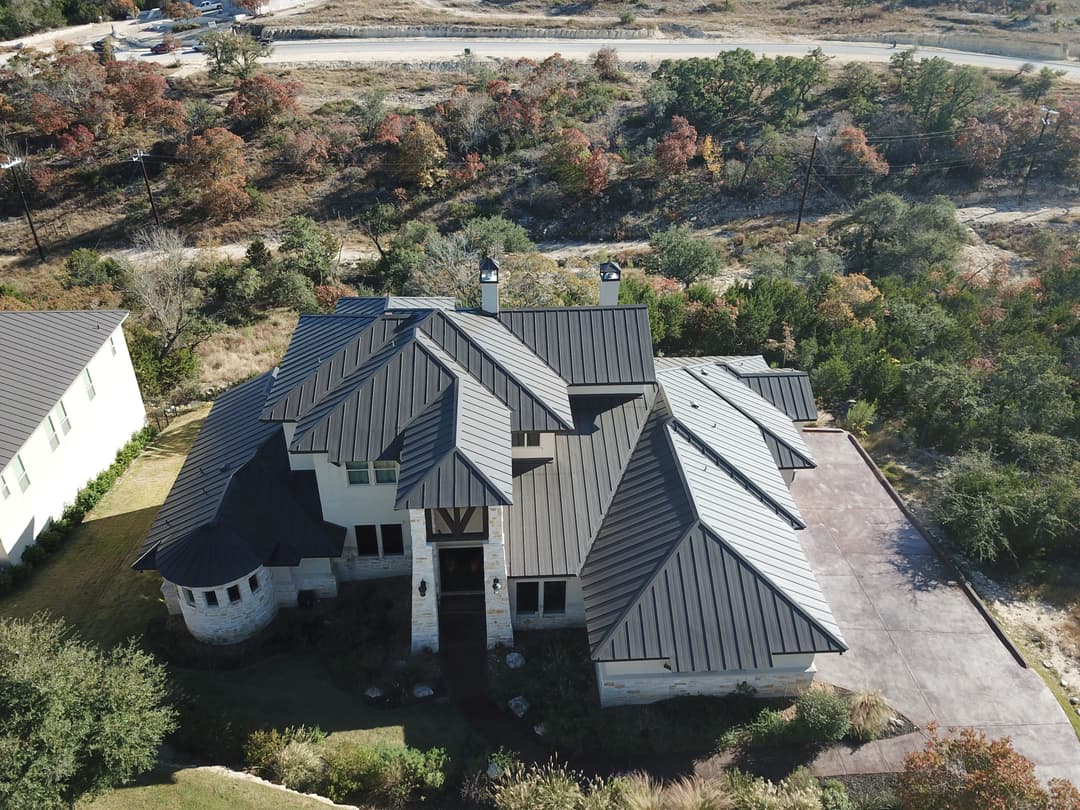 Aerial view of a modern house with a dark metal roof surrounded by trees.