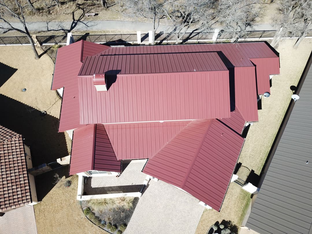 Aerial view of a modern house with a red metal roof and landscaped yard.
