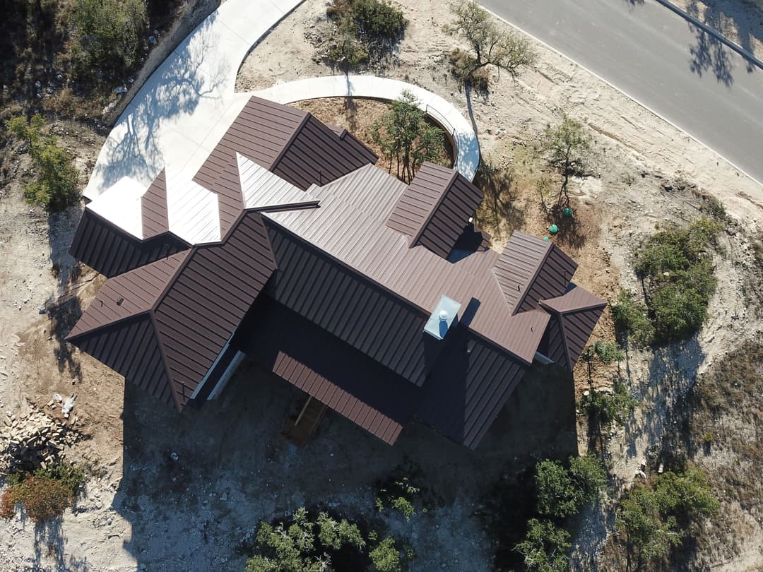 Aerial view of a modern home with a brown metal roof surrounded by landscaping.