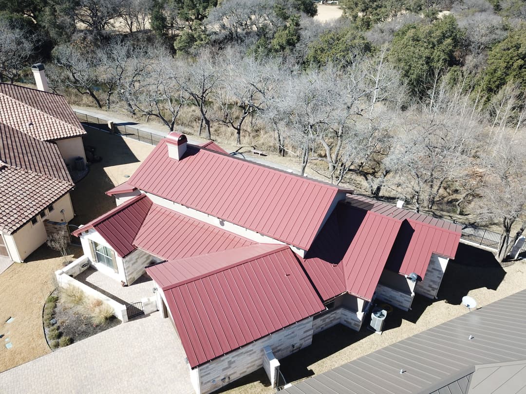 Aerial view of a modern home with a red metal roof surrounded by trees.