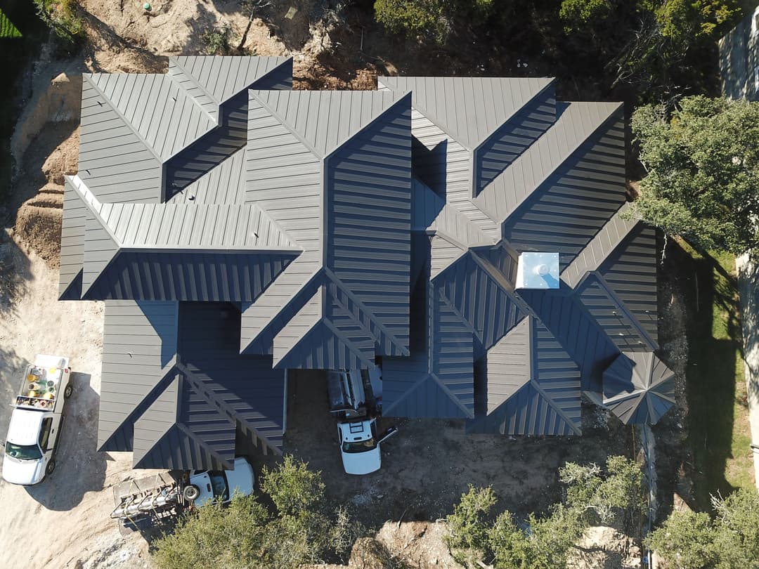 Aerial view of a modern house with multiple sloped roofs and construction vehicles nearby.