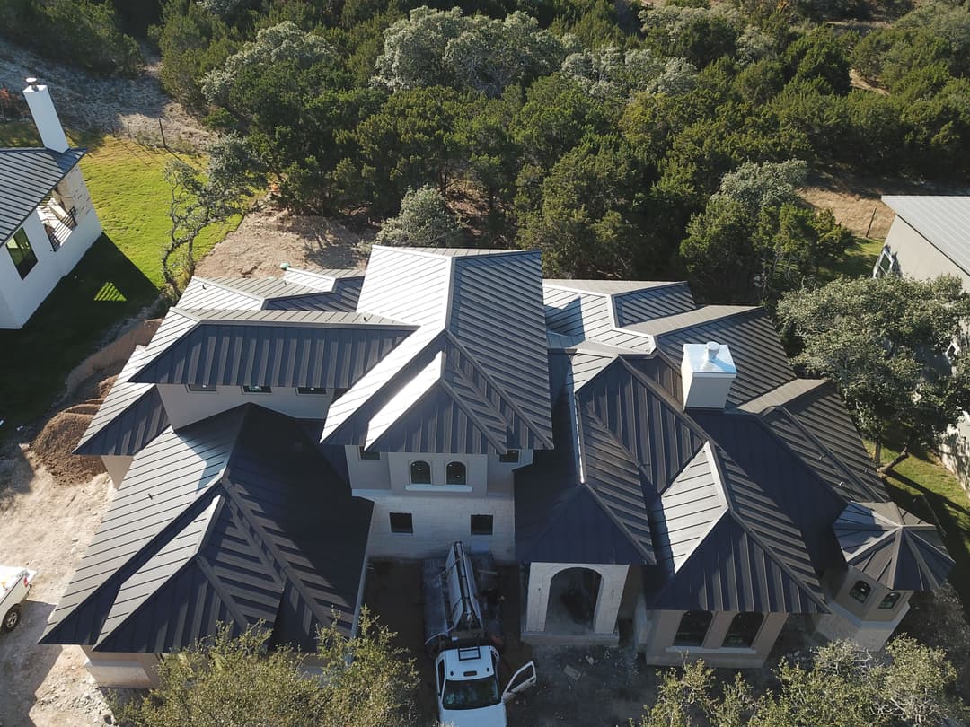 Aerial view of a modern home with a dark metal roof surrounded by greenery.