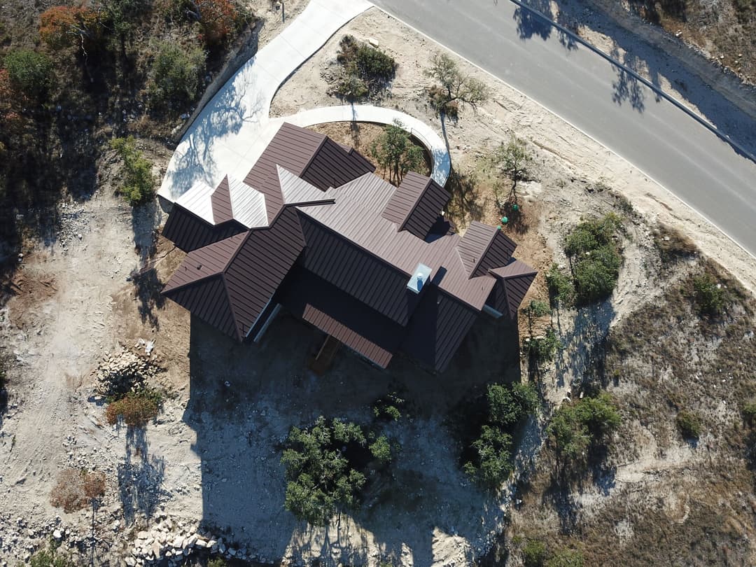 Aerial view of a modern brown roof house surrounded by dirt and sparse vegetation.