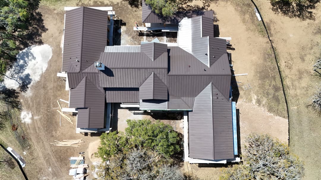 Aerial view of a large, multi-roofed residential construction with surrounding trees.
