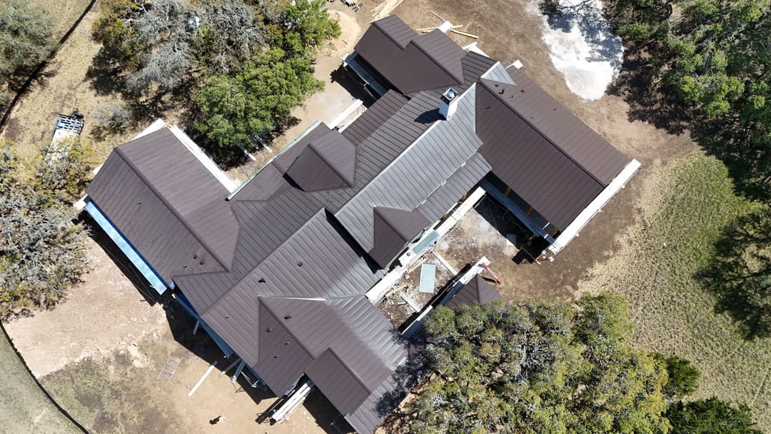 Aerial view of a large residential house with a brown roof and surrounding greenery.