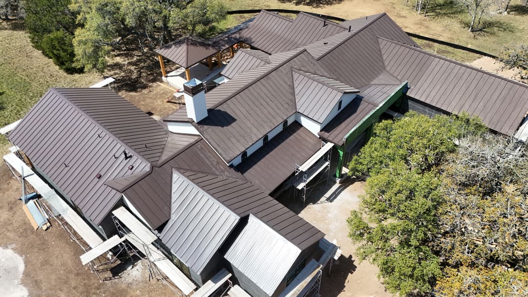 Aerial view of a modern home under construction with a metal roof and surrounding greenery.